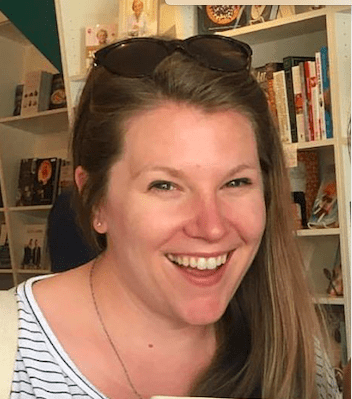 Smiling white woman facing the camera with a bookshelf in the background.